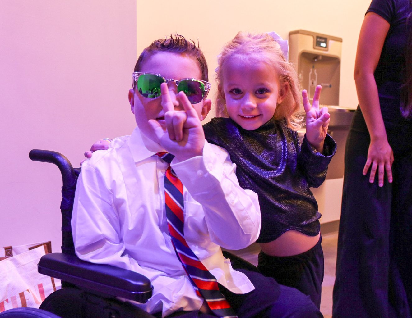 Two young models in sunglasses flashing peace signs backstage at the fashion show